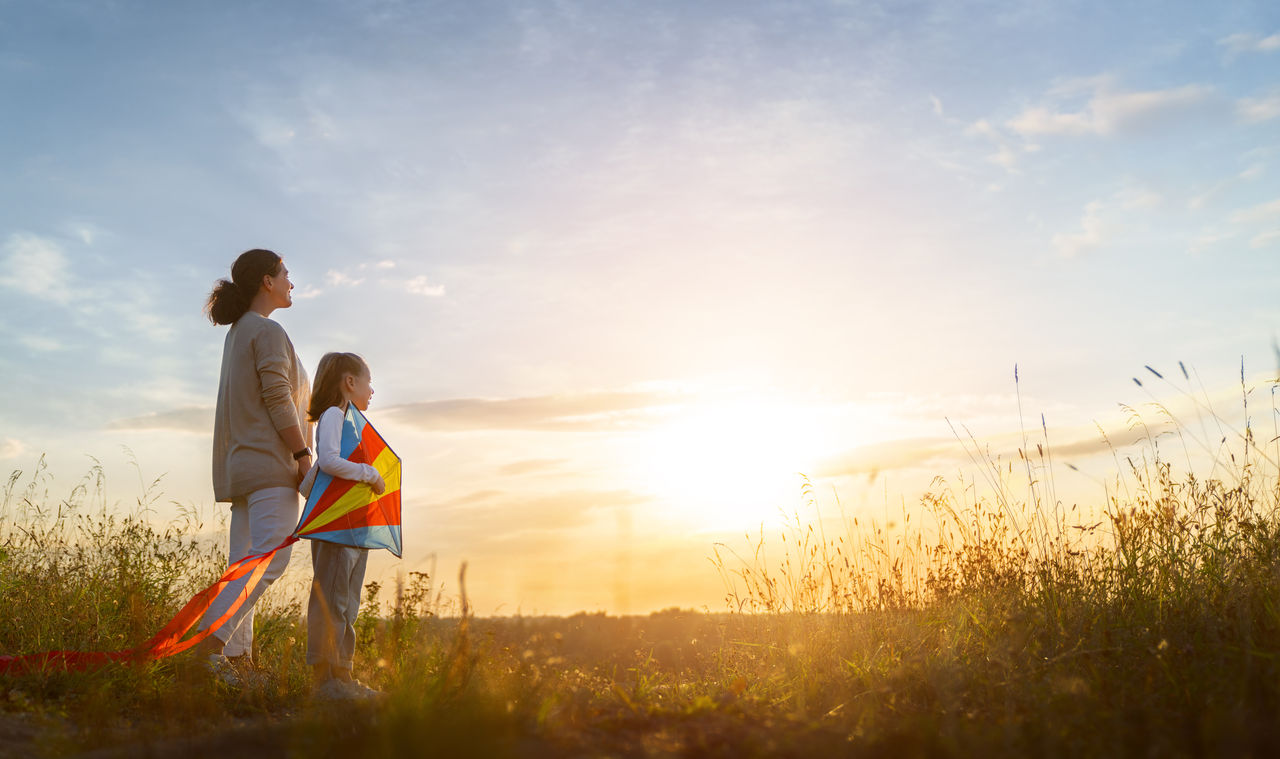 Happy family, mother and kid with kite are lokking at sunset. 